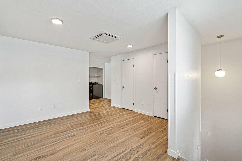 A room with white walls and wooden flooring with a black trash can and a light hanging from the ceiling.