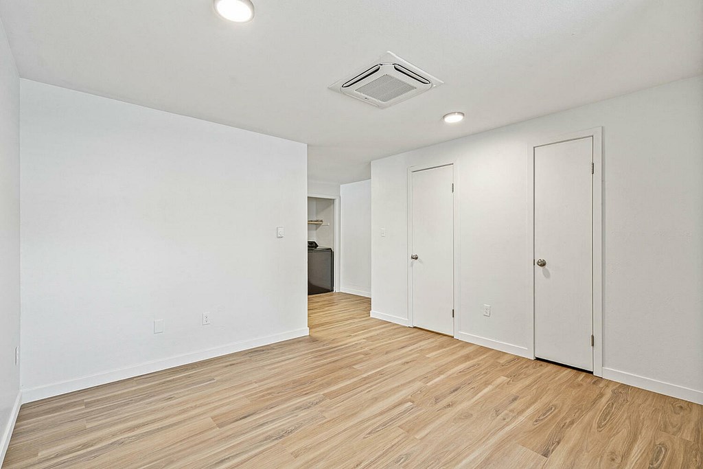 A room with white walls and wooden flooring with a white door on the right.