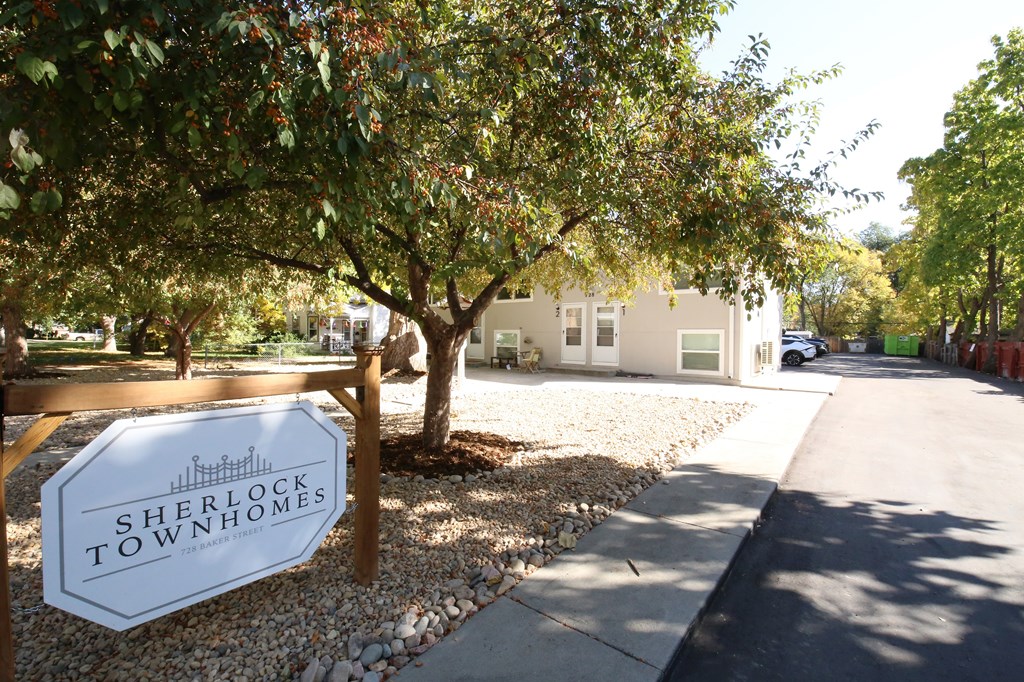 A sign for Sherlock Townhomes is in front of a tree.