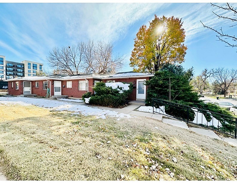 A small building with a red brick exterior is surrounded by a grassy area with a tree and a sidewalk.