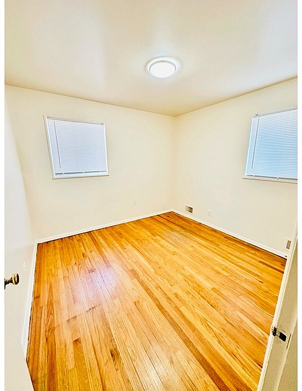 A room with wooden flooring and two windows.