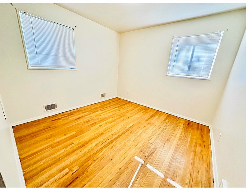 A room with wooden flooring and two windows.
