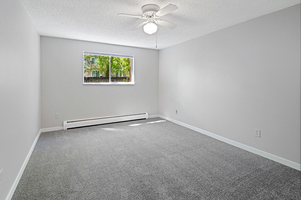 A room with a ceiling fan and a window with a view of trees.