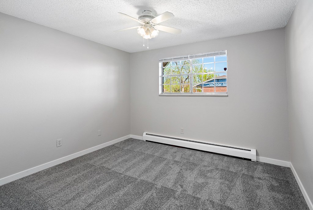 A room with a ceiling fan and a window with a view of a building outside.