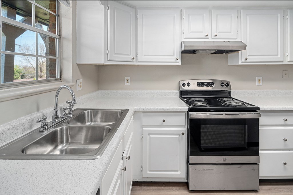 A kitchen with white cabinets and a stainless steel sink and oven.