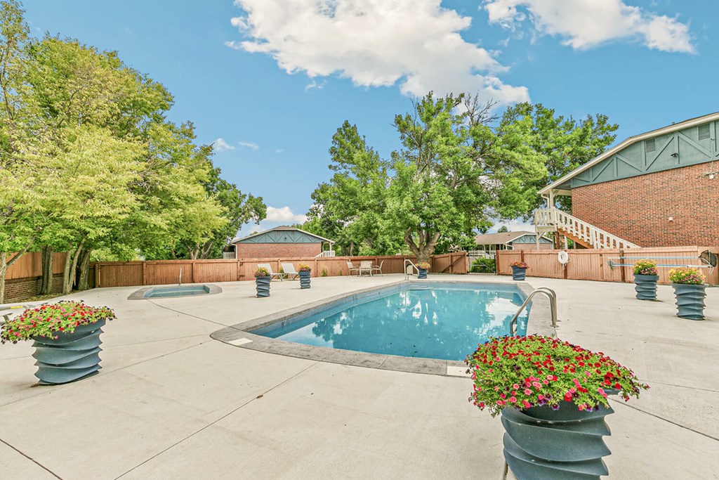 A pool surrounded by trees and concrete planters with flowers.