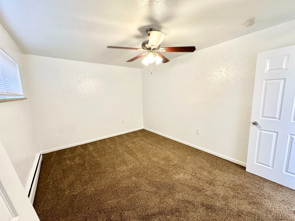 A room with a ceiling fan and brown carpet.