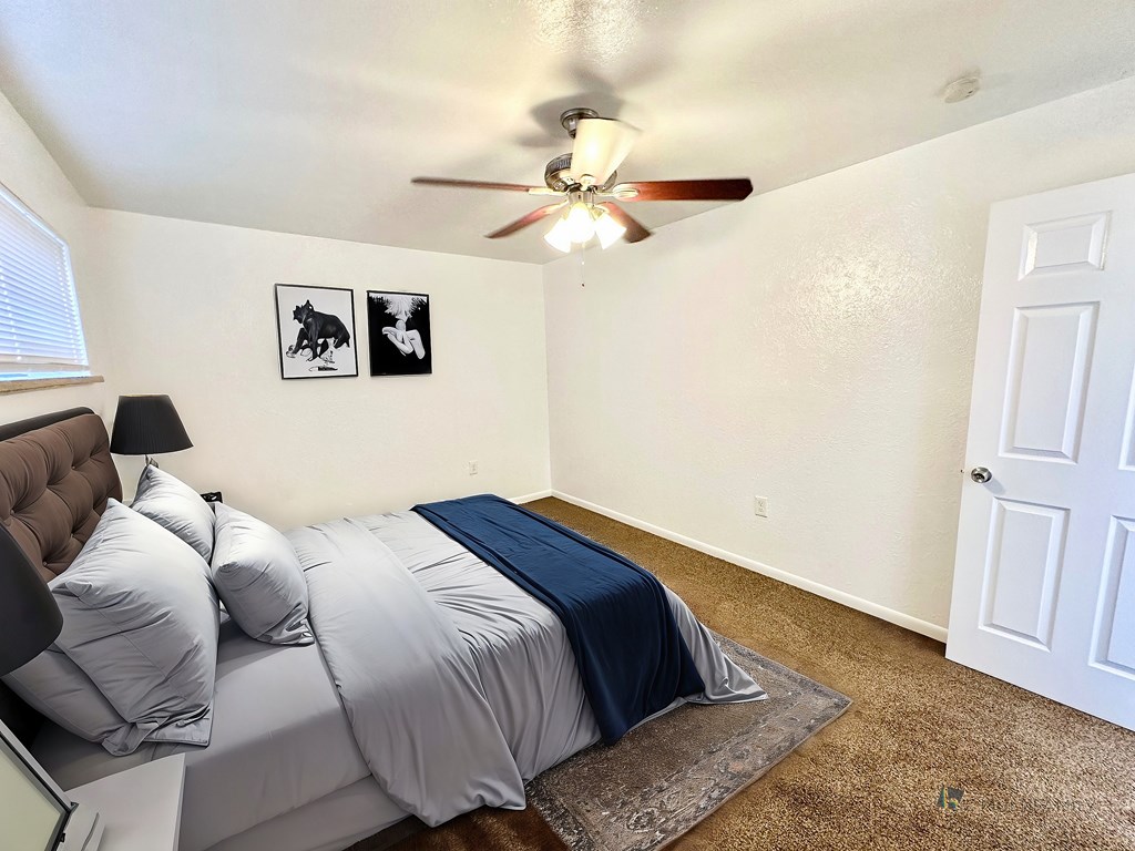 A bedroom with a bed, pillows, a ceiling fan, and two pictures on the wall.