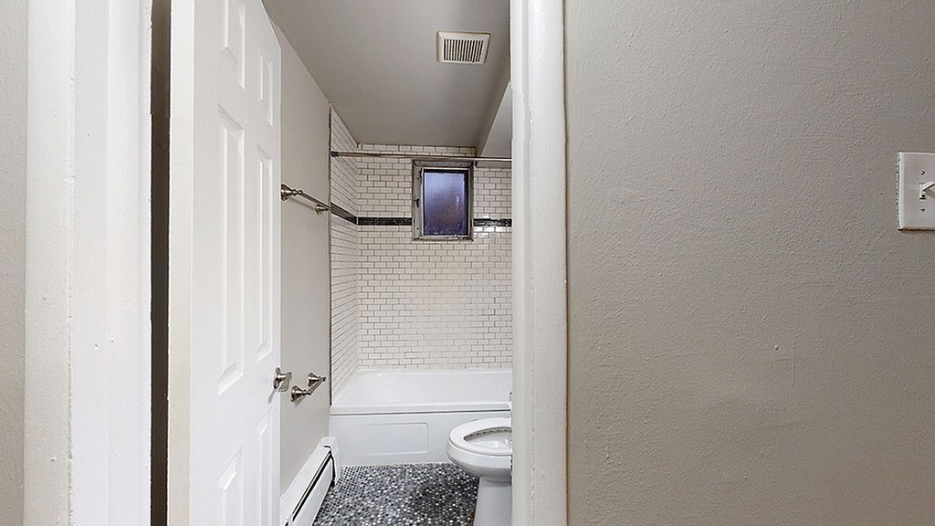 A white door is open to a small bathroom with a toilet and a shower.