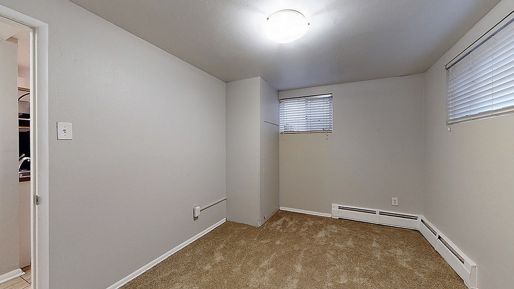 A room with a carpeted floor and a window with blinds.