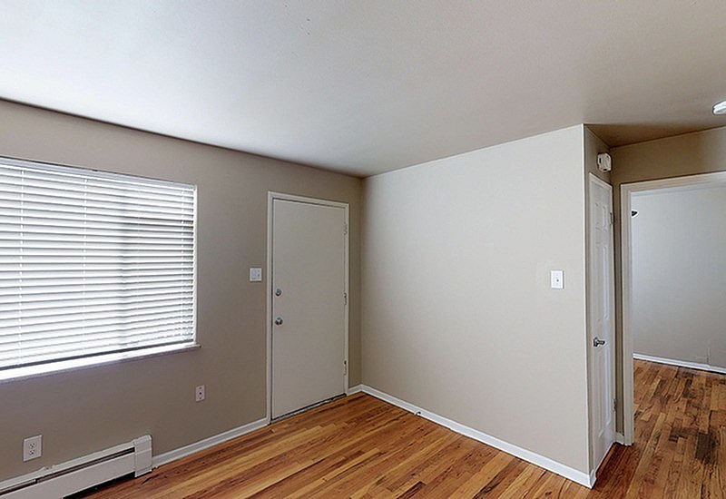 A room with a window, a door, and a wooden floor.