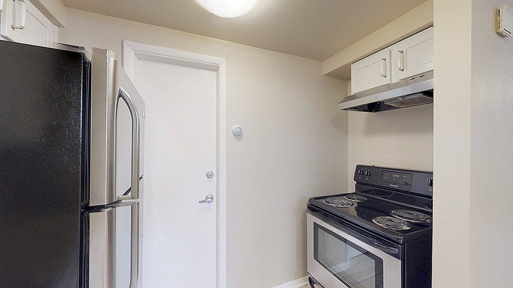 A black refrigerator is on the left of a white door in a kitchen.
