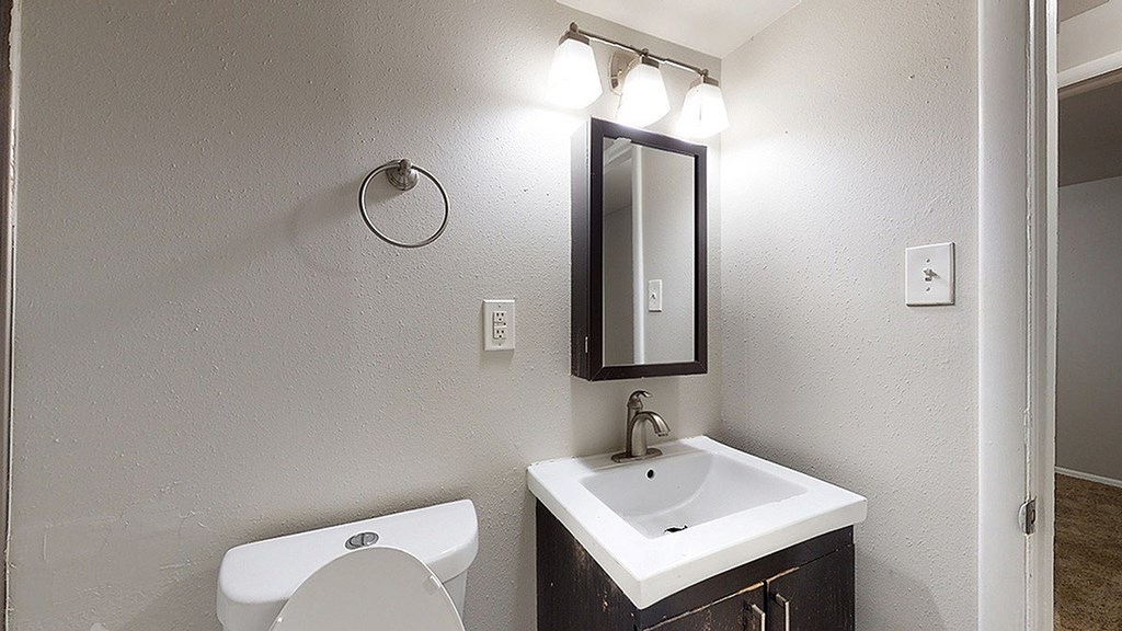 A bathroom with a toilet, sink, mirror and lights.