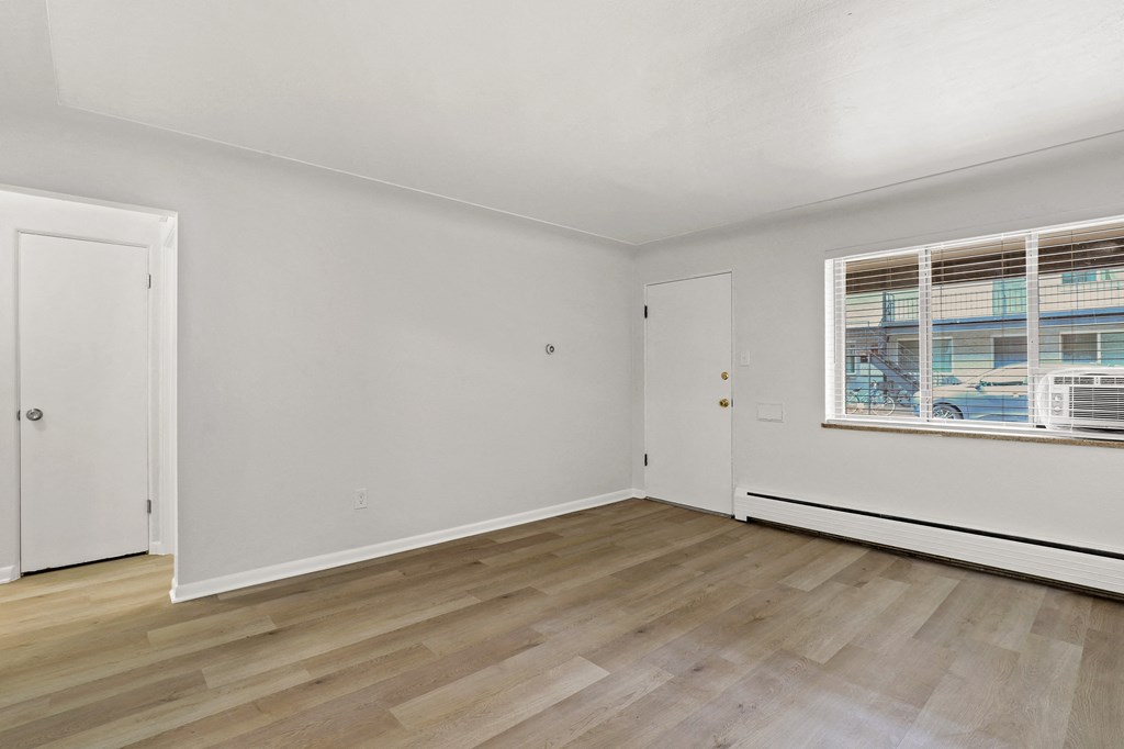 A room with white walls and wooden flooring with a window on the right side.