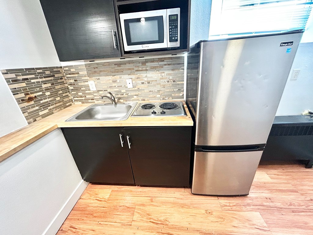 A kitchen with a stainless steel refrigerator, a sink, and a microwave above it.