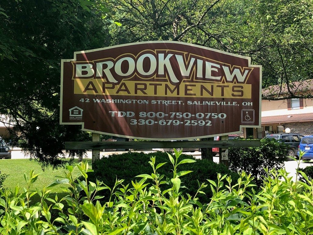 A brown and white sign for Brookview Apartments sits in front of some greenery.