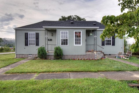 A grey house with a porch and a tree in front.