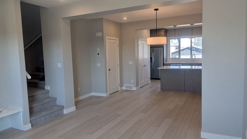 A spacious room with wooden flooring and a staircase on the left side.