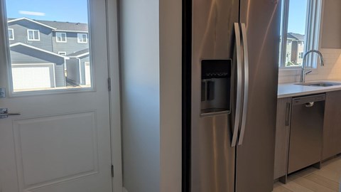 A stainless steel refrigerator in a kitchen with a view of a residential area outside the window.