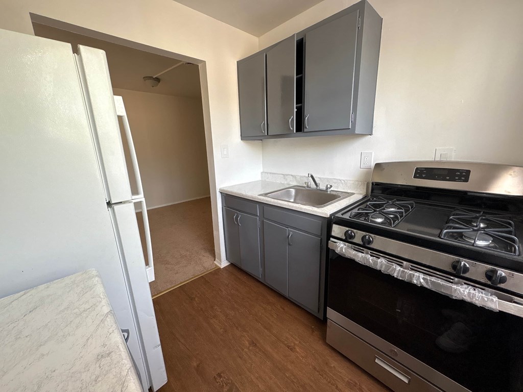 A kitchen with a white refrigerator, a stove, and grey cabinets.