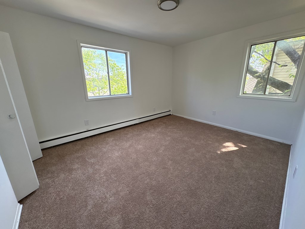 A room with carpeted floor and two windows.