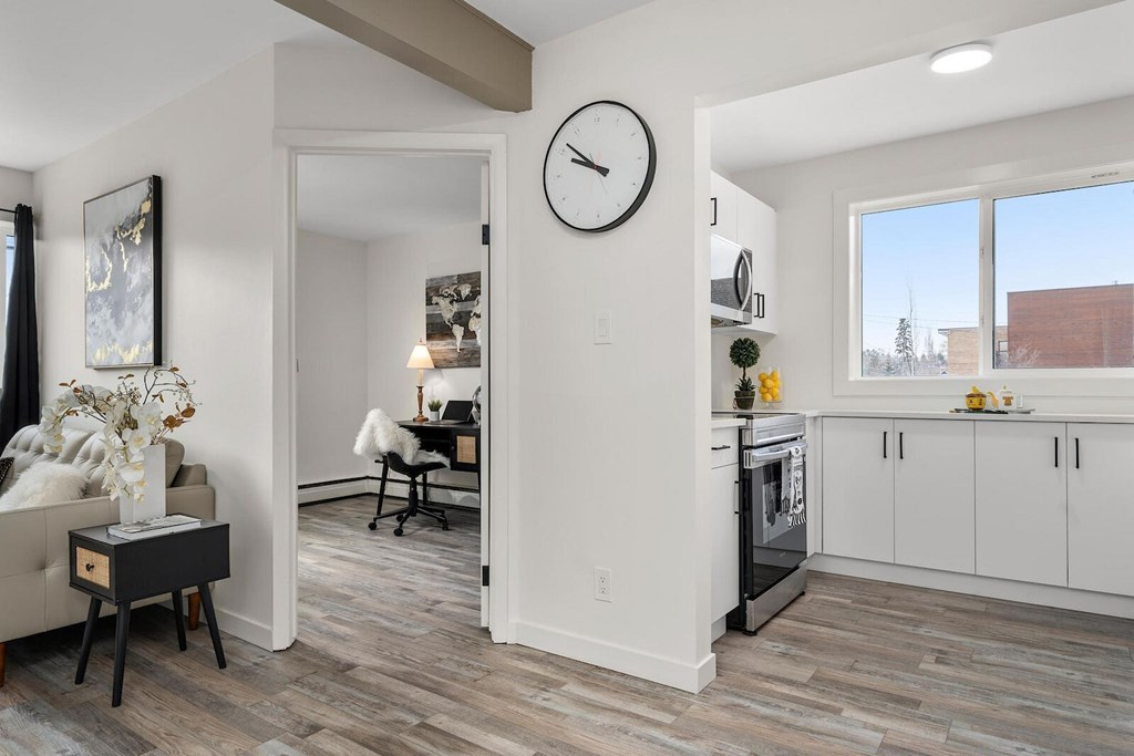 A living room with a couch, a chair, a table with a vase, and a clock on the wall.
