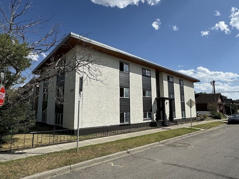 A building with a white facade and a brown roof is situated on a street corner.