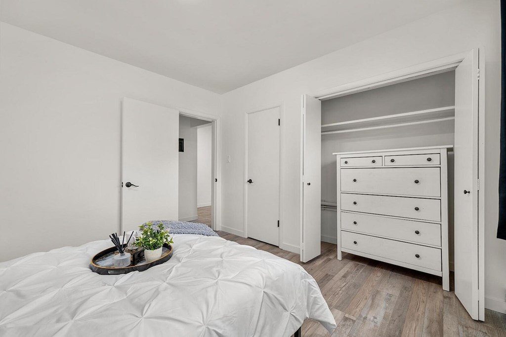 A white bedroom with a bed, dresser, and wardrobe.