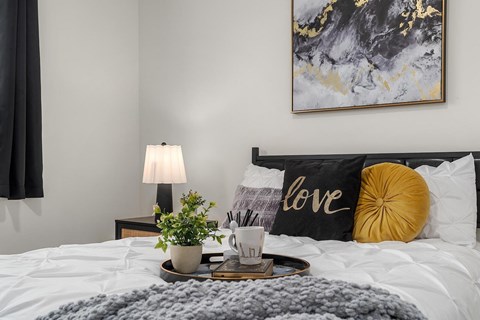 A bedroom with a bed, a lamp, a plant, and a pillow with the word "love" written on it.