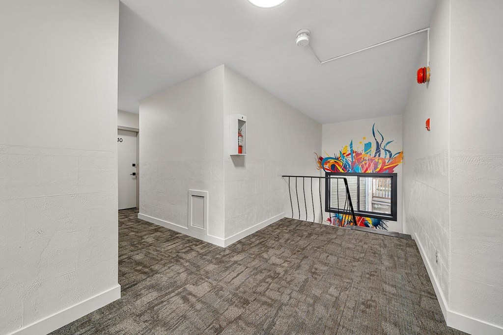 A room with a grey carpet and a white wall with a fire extinguisher on it.
