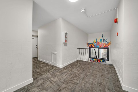 A room with a grey carpet and a white wall with a fire extinguisher on it.