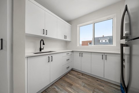 A kitchen with white cabinets and a window overlooking a house.