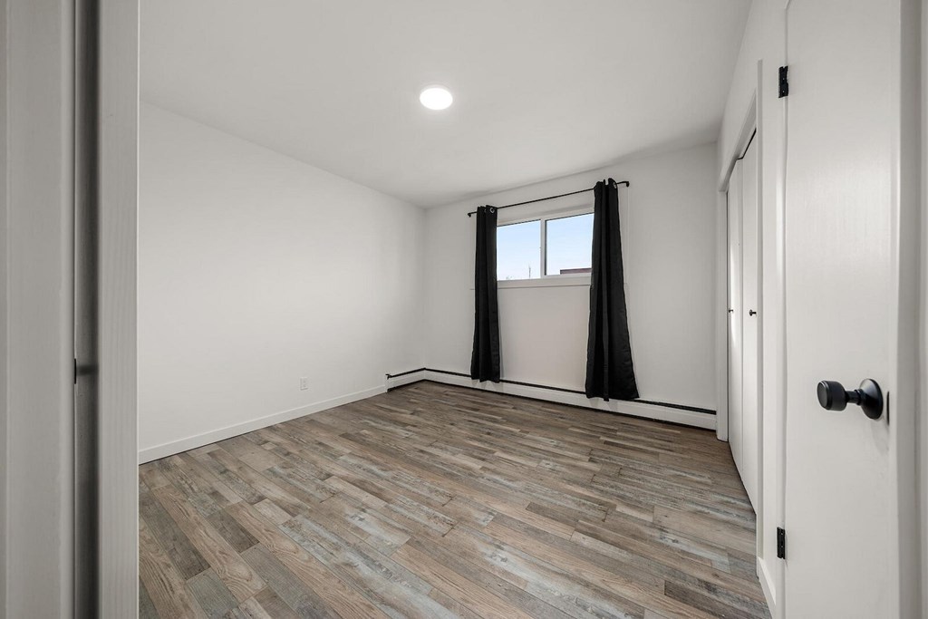 A room with a wooden floor and a window with black curtains.
