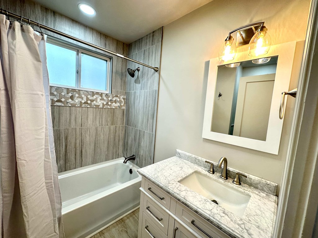 A bathroom with a marble countertop and a white bathtub.