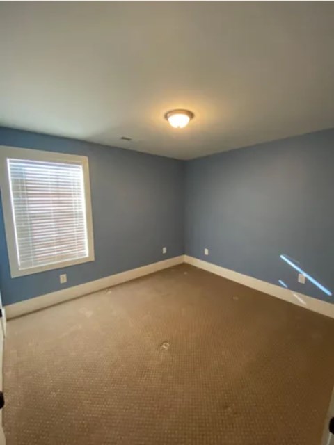 A room with a carpeted floor and a window with blinds.