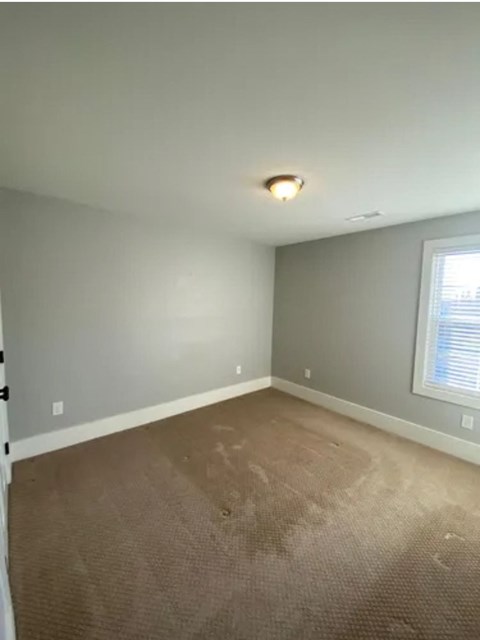 A room with a carpeted floor and a window with blinds.
