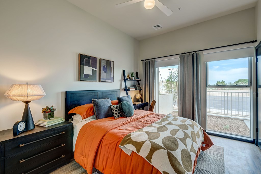 A bedroom with a bed, nightstand, and a window with a view of a fence and trees.