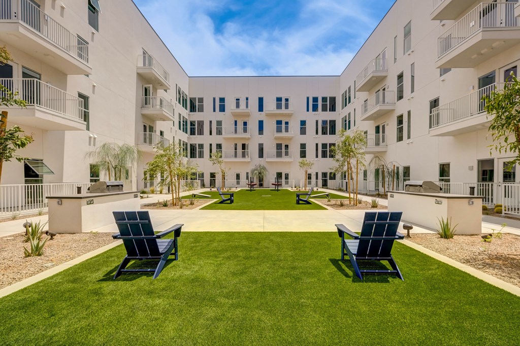 Two blue chairs are placed on a green lawn in front of a white building.