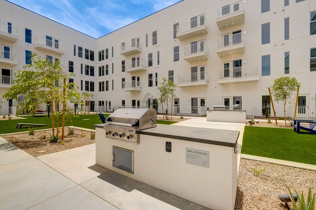 A modern outdoor kitchen with a grill and sink is in front of a white apartment building.