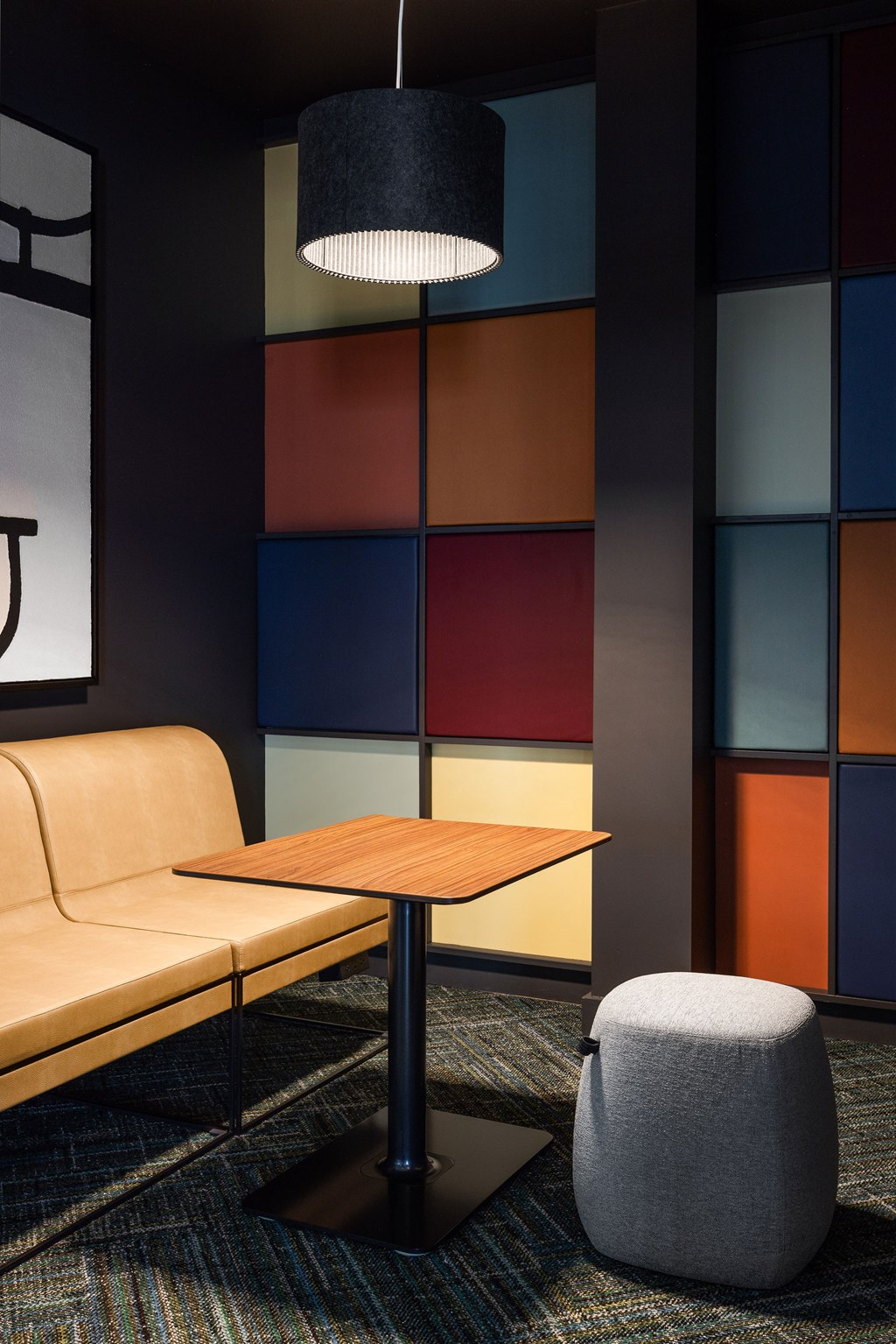 A modern living room with a tan couch, a grey ottoman, and a wooden table.