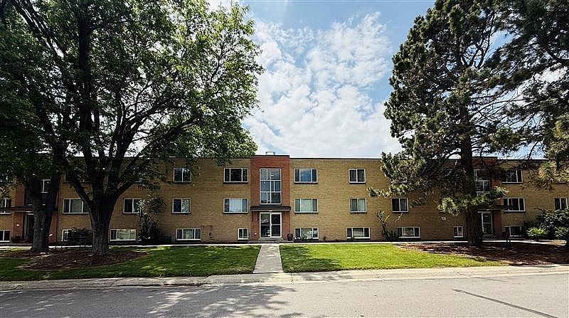 Apartment building with trees in front and a clear sky above.