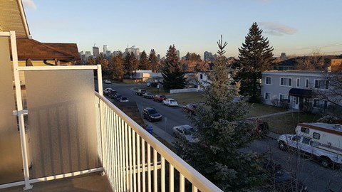 A view from a balcony overlooking a parking lot and trees.