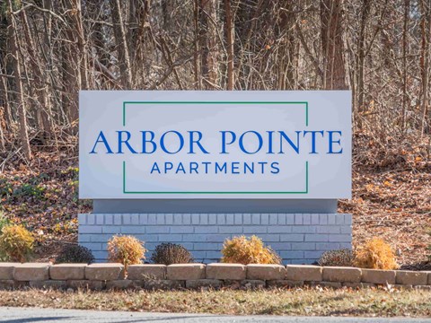 A sign for Arbor Pointe Apartments stands in front of a wooded area.
