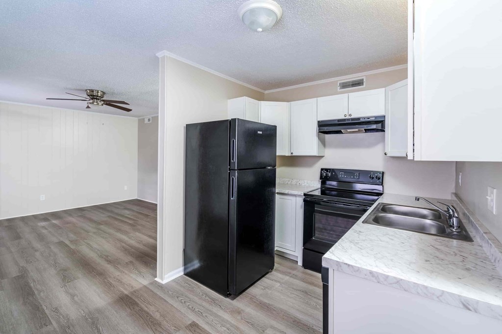 A black refrigerator stands in a kitchen with a white counter and a fan on the ceiling.