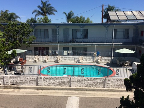 A pool surrounded by a stone wall and chairs with umbrellas.