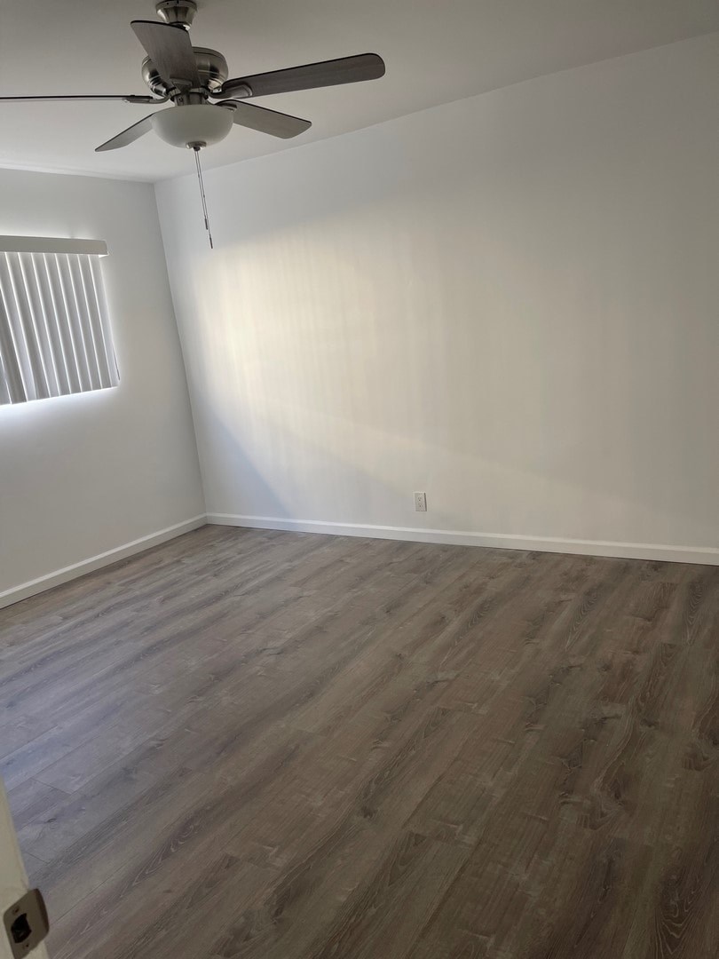 A room with a ceiling fan and wood flooring.