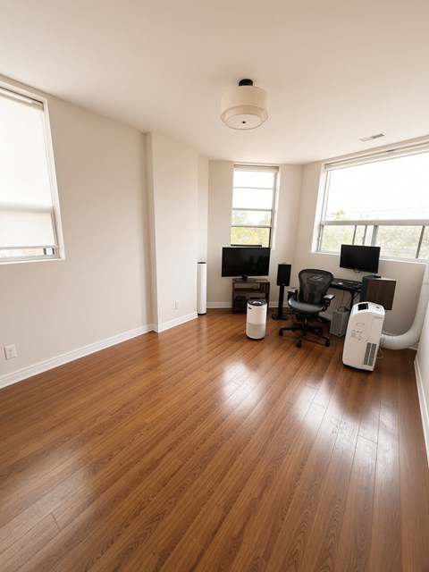 A room with wooden floors and two computer desks with chairs.