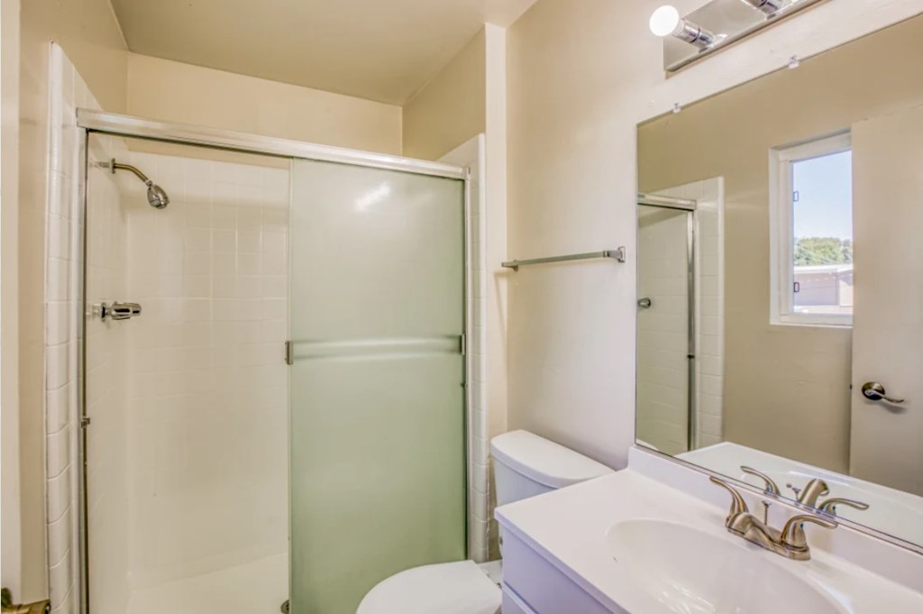 A white bathroom with a glass shower door and a white toilet.