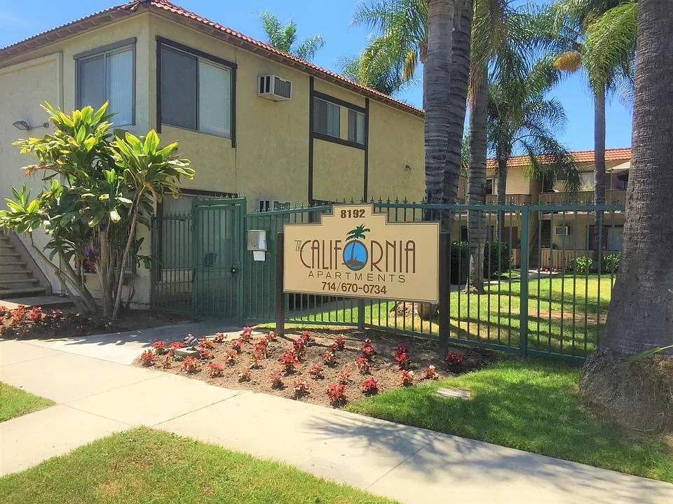 A sign for Calvonia Apartments is in front of a building with a green fence and trees.