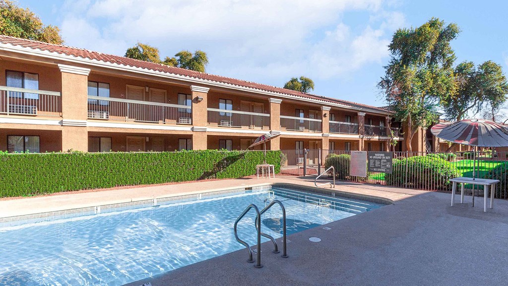 A swimming pool is in front of a building with a red roof.